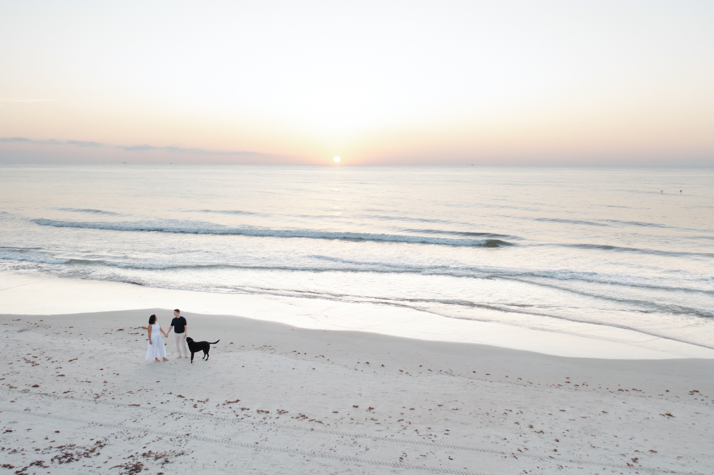 Ryan and Gabrielle walking on the beach at sunset with their dog Mac